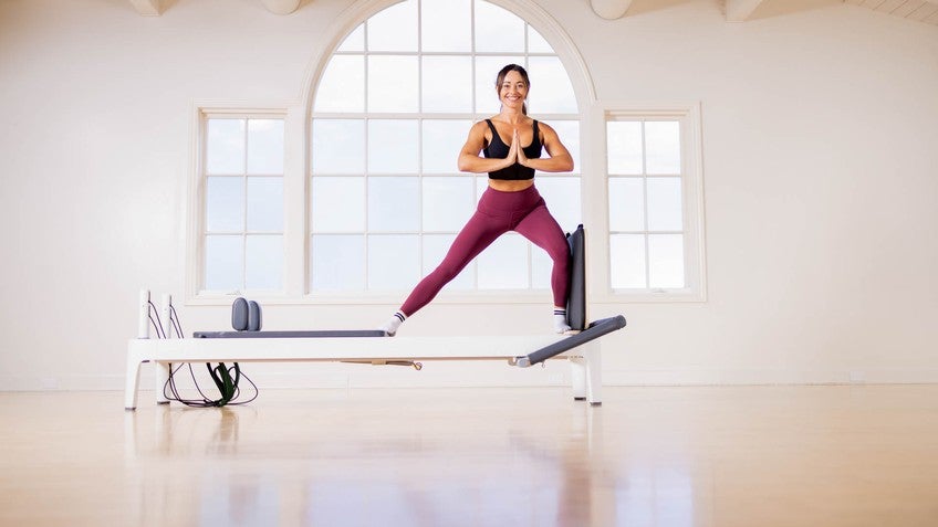 Side view of fit woman doing legs exercise with resistance ropes on Pilates  reformer in gym